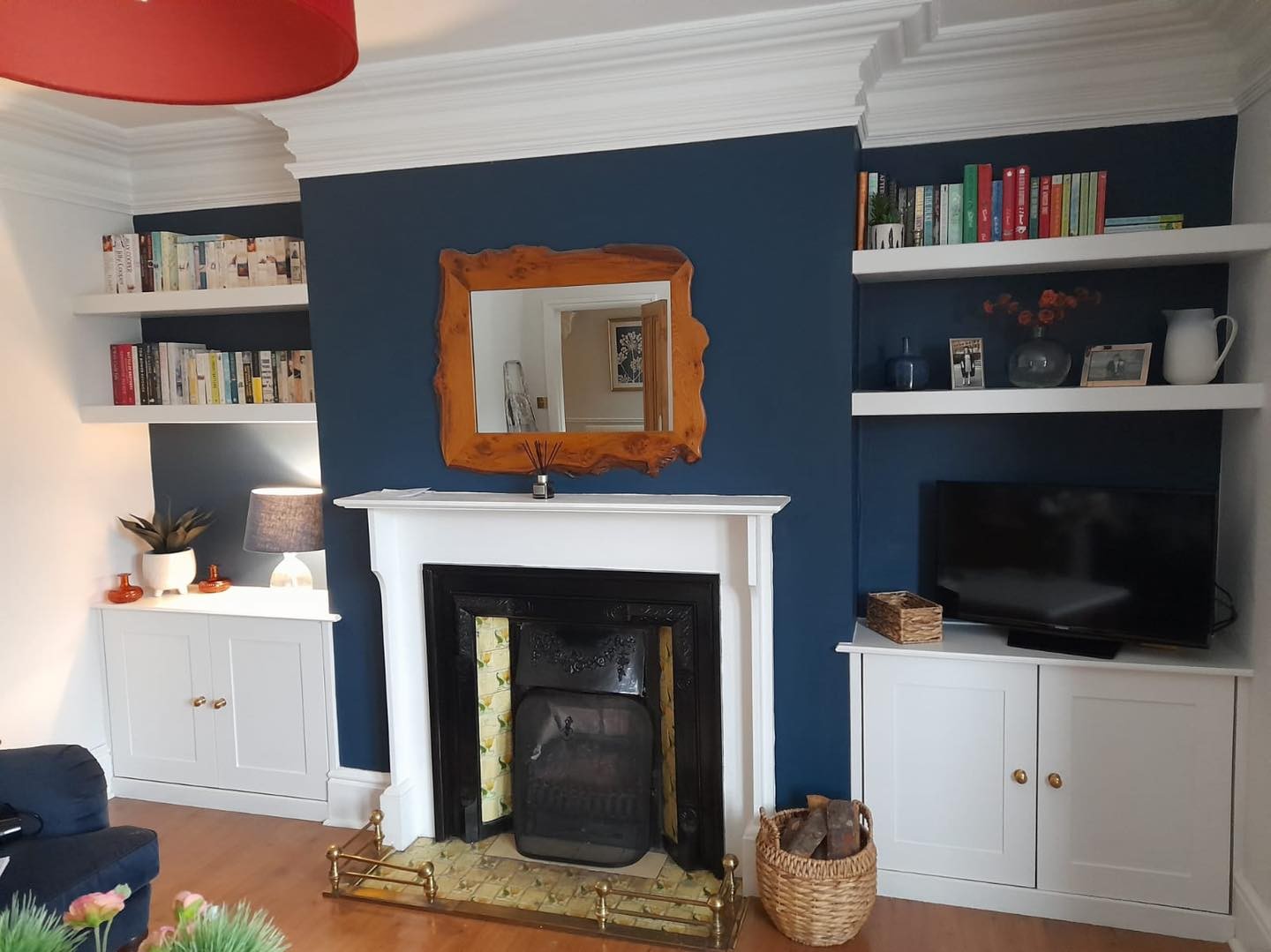 Painted alcove cupboards and shelving either side of a fireplace in a navy room
