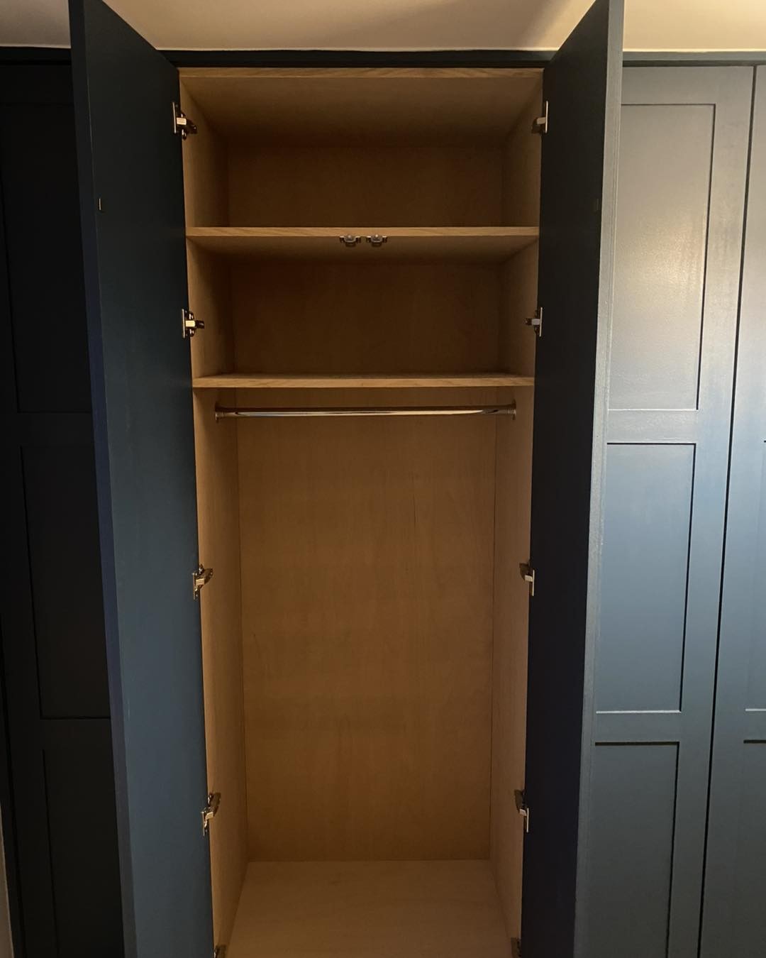 Navy shaker wardrobe open to show shelves and an oak ply interior