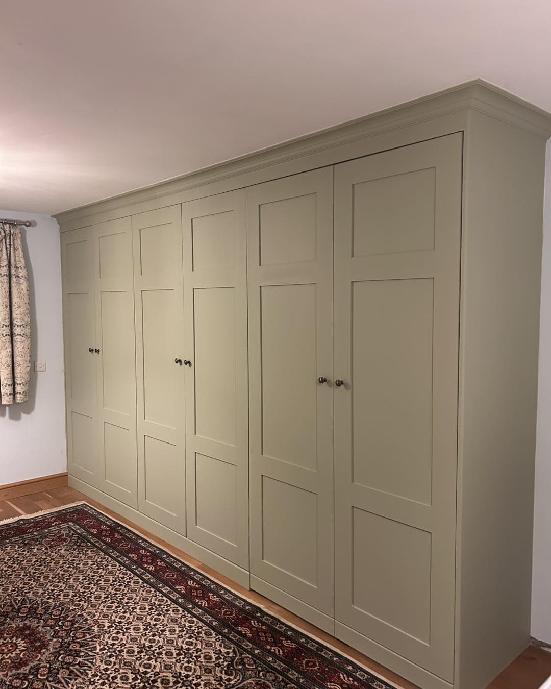 A long run of sage green shaker built-in wardrobes